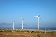 Três grandes aerogeradores em um campo com um céu azul claro ao fundo.